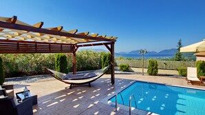 Ett poolområde med en pergola, en hängmatta och utemöbler.