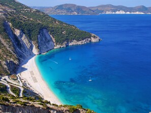 A coastal landscape with a beach, cliffs, and clear blue sea.