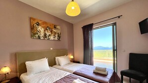 Ett hotellrum med två sängar, en tavla på väggen, en balkong med utsikt och en tv som är monterad på väggen.