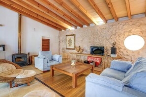 Un salon chaleureux avec un mur en pierre, des poutres en bois, une cheminée et des sièges confortables.
