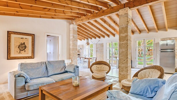 A living room with a wooden ceiling, a sofa, a coffee table, and a wicker chair.