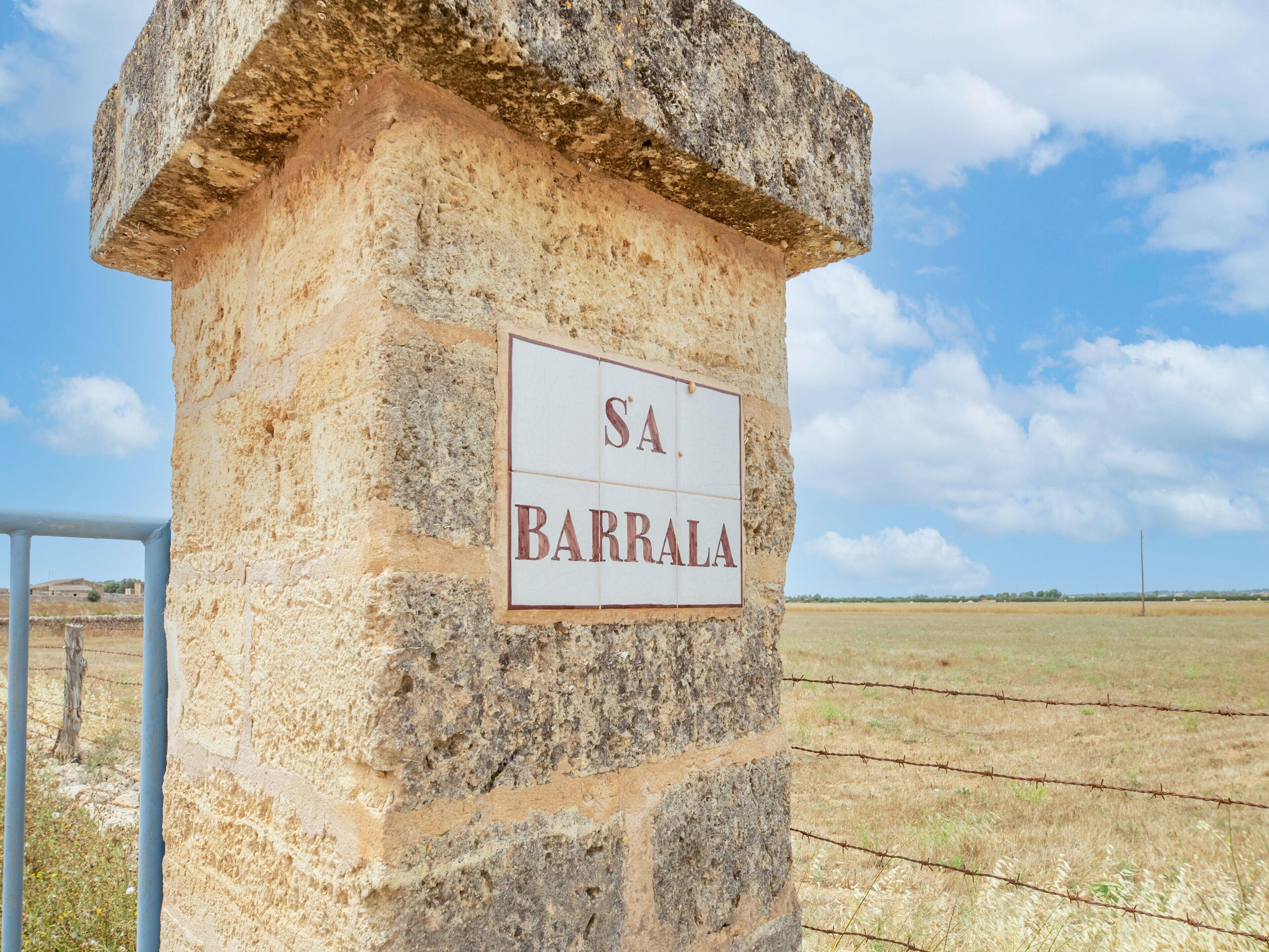 A stone pillar with a sign reading 'SA BARRALA' in a rural setting.