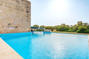 A swimming pool with a stone wall and a view of greenery and a tower in the distance. - Holiday Home "Gallinero" at Possessió Sa Barrala with Private Access to Es Trenc Beach (Campos)