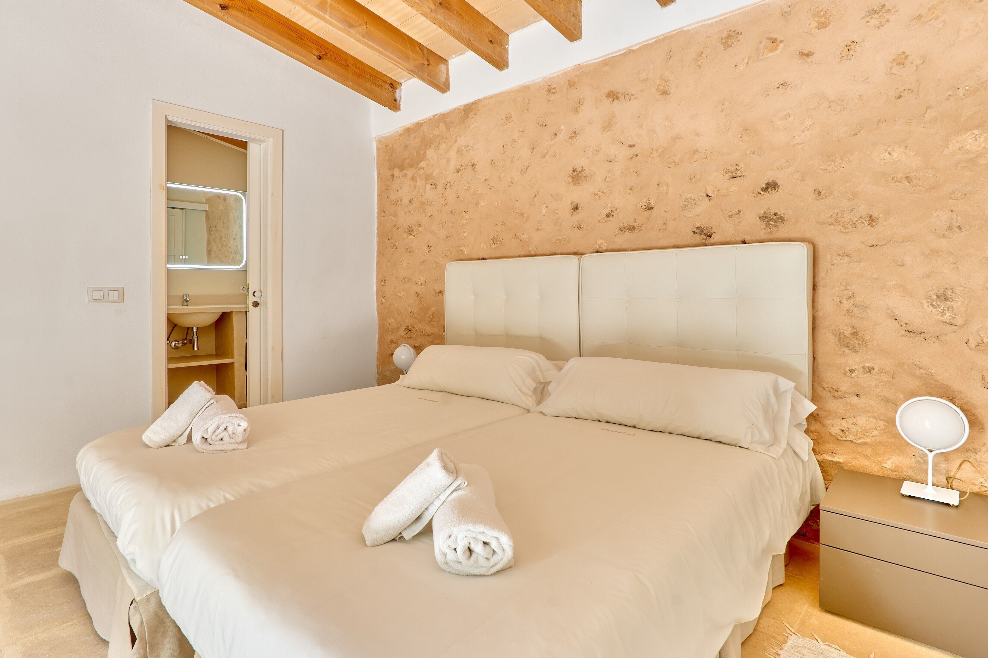 Un dormitorio con cama, dos almohadas, una mesita de noche con lámpara y un espejo.