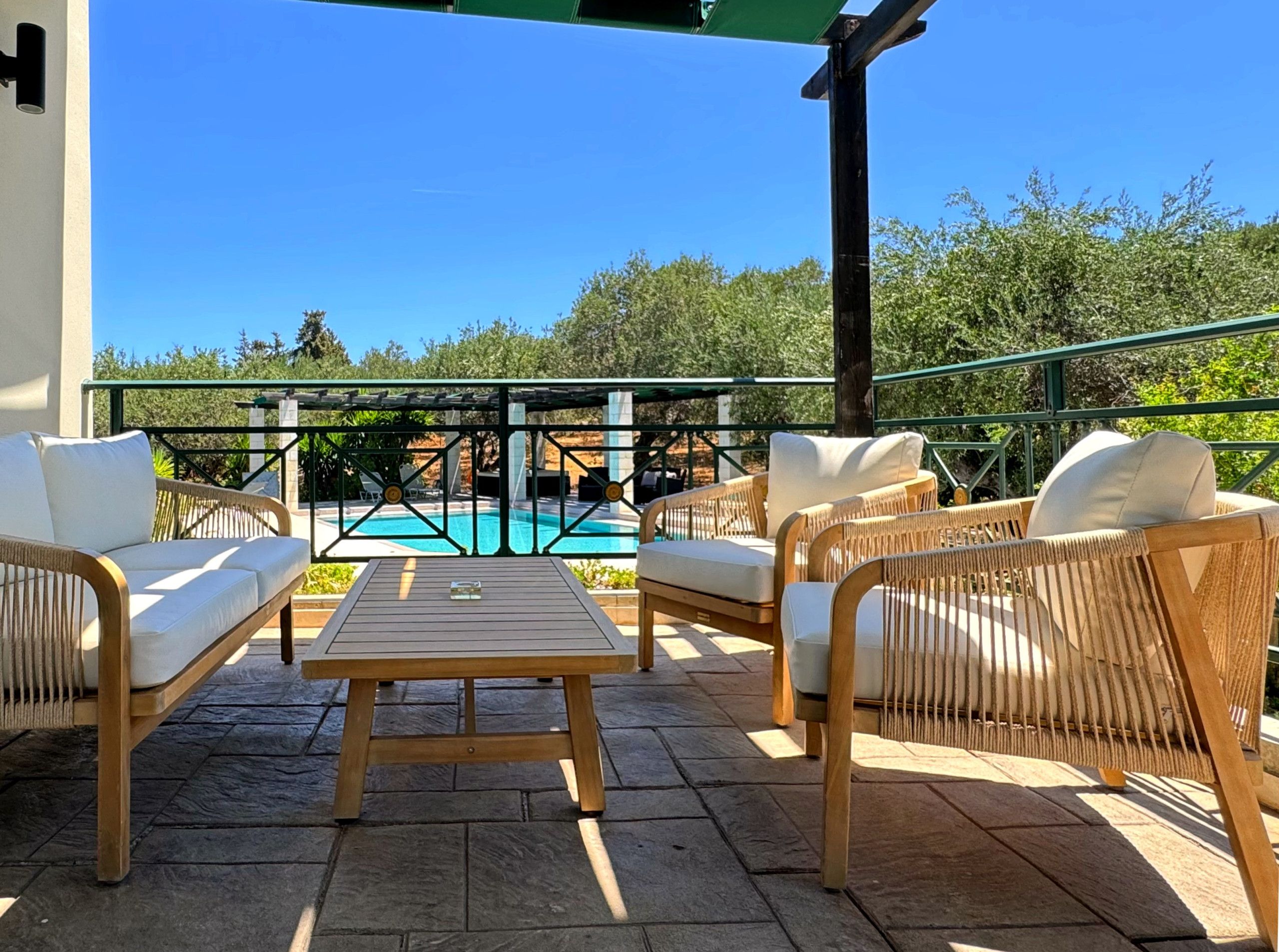 An outdoor patio with wicker furniture, a wooden table, and a view of a swimming pool.