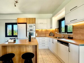 Une cuisine moderne dotée d’un îlot central en bois, d’appareils électroménagers intégrés et offrant une vue sur la verdure environnante.