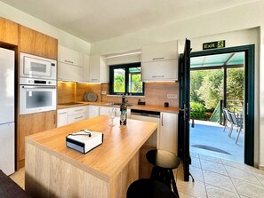 A modern kitchen with built-in appliances, a wooden island, and a view of the outdoors.