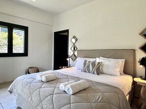 A bedroom with a large bed, a bedside table, a nightstand, a window, and a door.