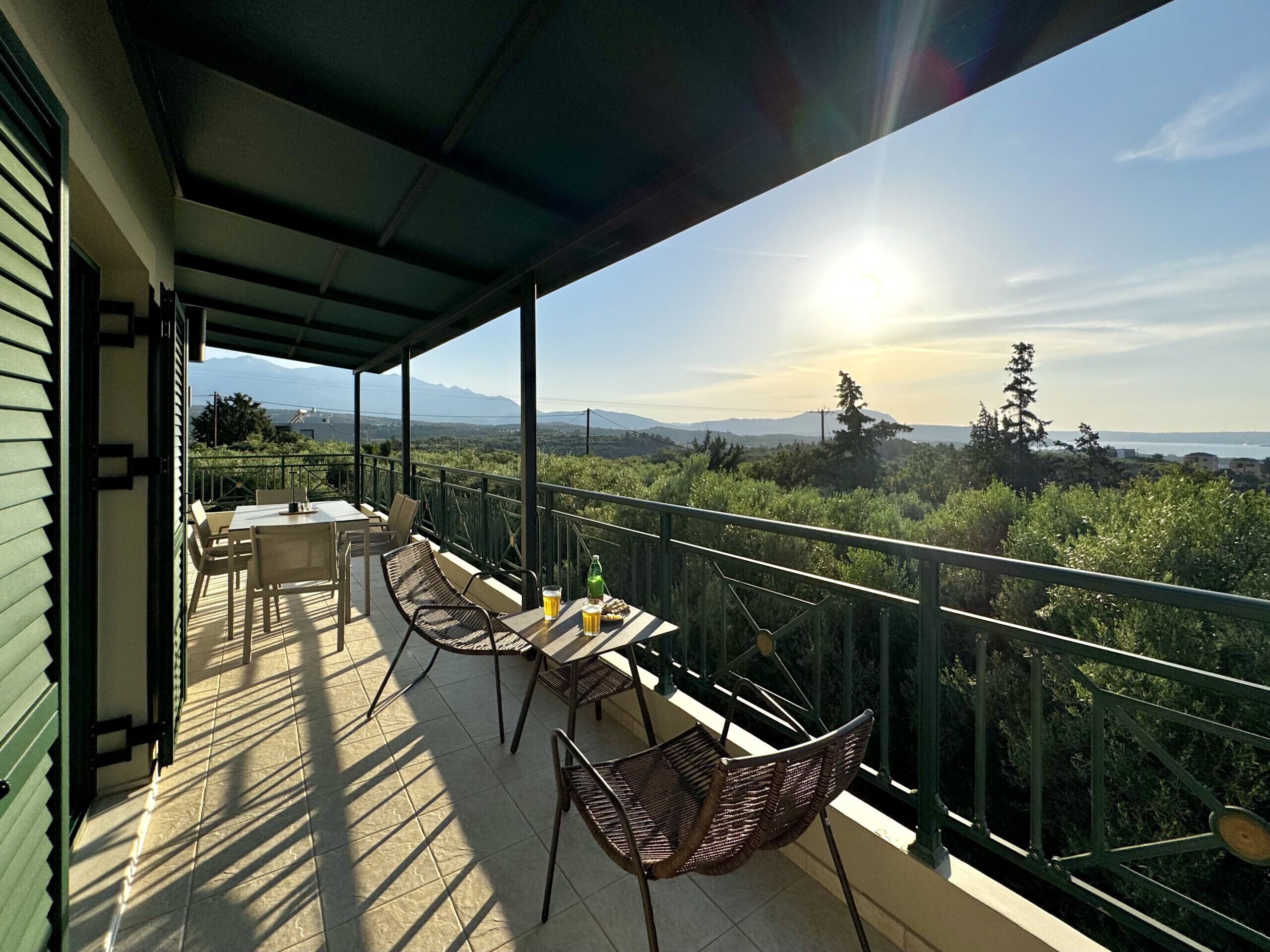 A balcony with a table and chairs, overlooking a landscape with trees and distant mountains.
