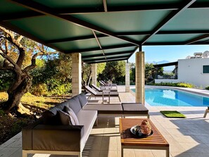 Un espace aménagé au bord de la piscine, comprenant un coin salon couvert, une piscine et une vue sur une montagne.