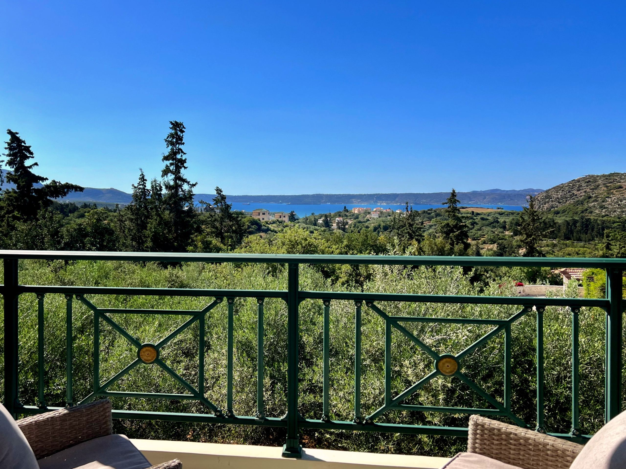 A balcony with a view of a coastal landscape, including trees and distant buildings.