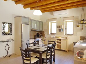 A kitchen with wooden cabinets, a dining table with chairs, a hanging light fixture, and a window. - Villa Olivia (Vrises)