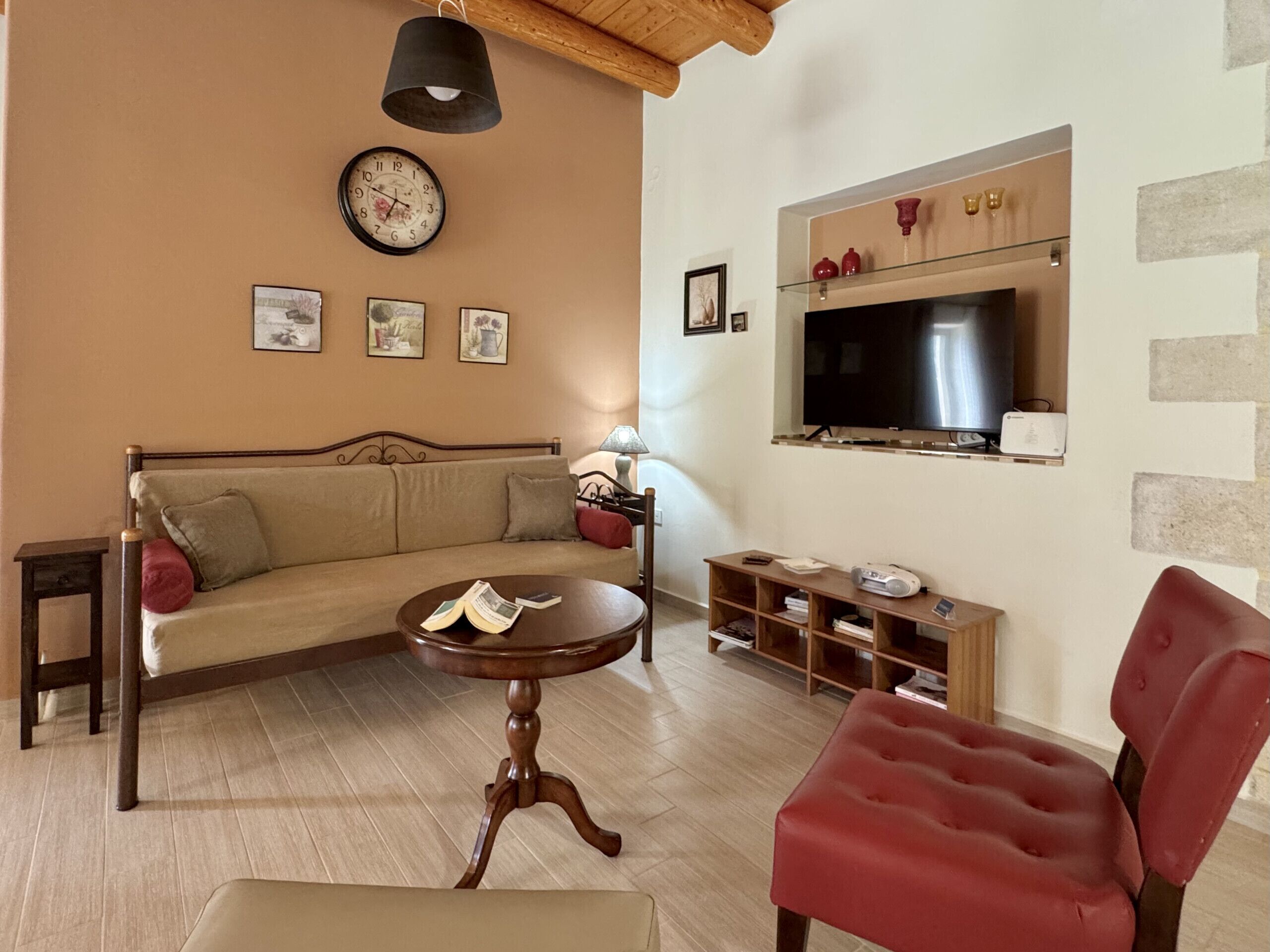 A living room with a sofa, a red chair, a wooden coffee table, a TV, and a wall clock.