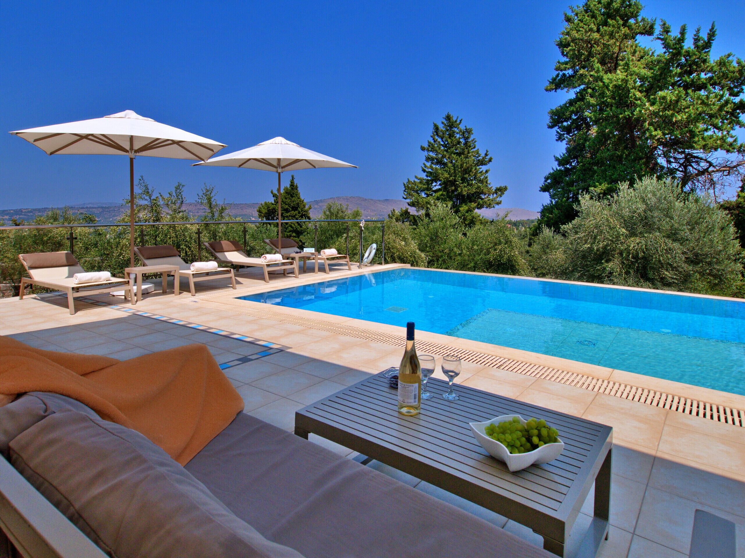 A poolside area with lounge chairs, umbrellas, and a table with a bottle and glasses.