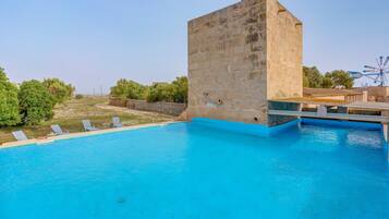 A swimming pool with a stone structure, lounge chairs, and a Ferris wheel in the background.