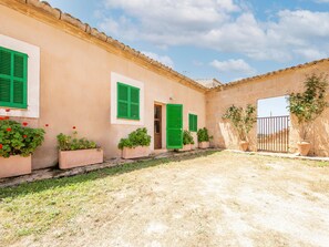 Une cour intérieure avec un bâtiment doté de volets verts, de plantes en pot et d’un portail.