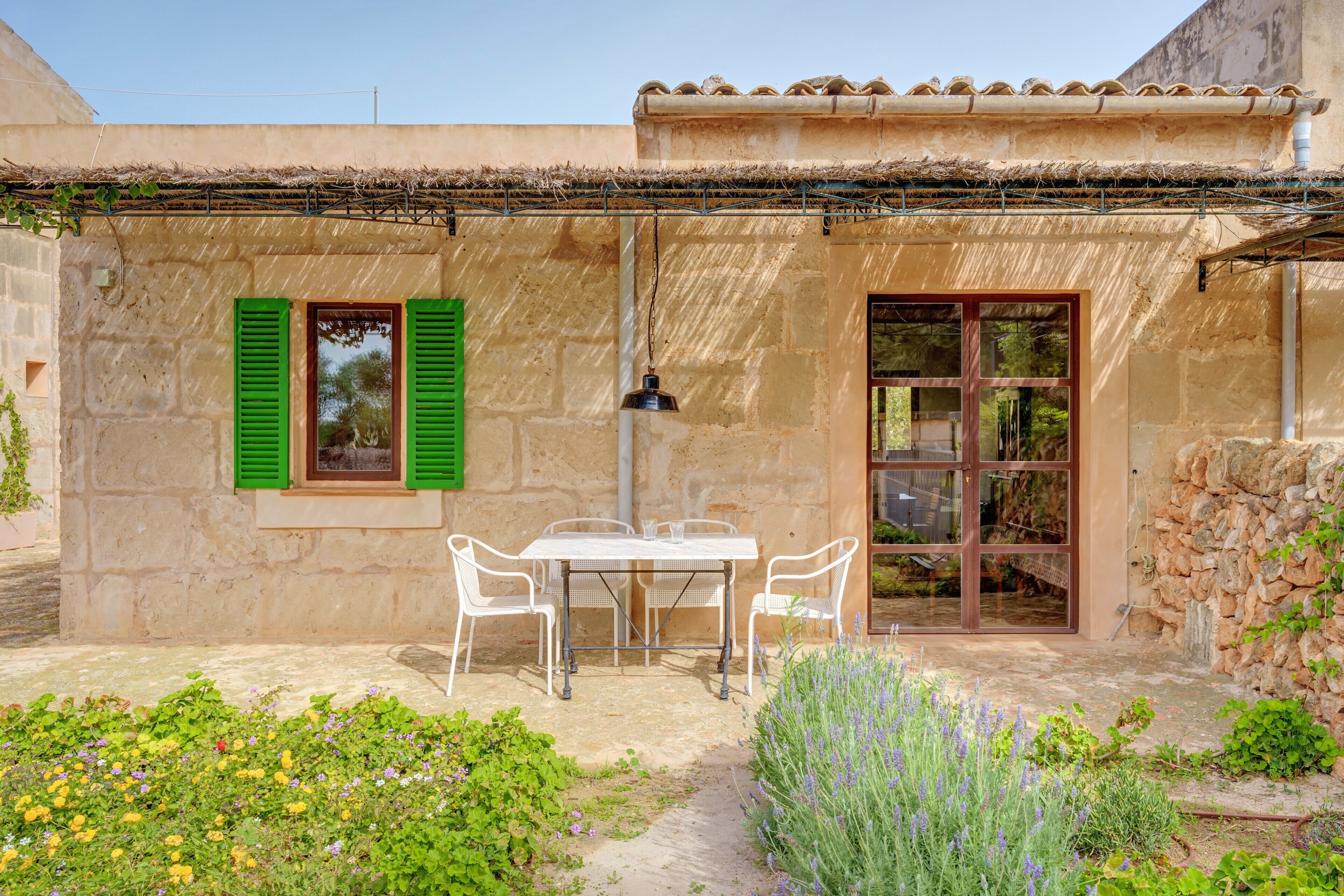 Un edificio de piedra con una mesa, sillas, una ventana con contraventanas verdes y una puerta.