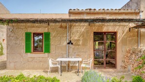 Un edificio de piedra con una mesa, sillas, una ventana con contraventanas verdes y una puerta.