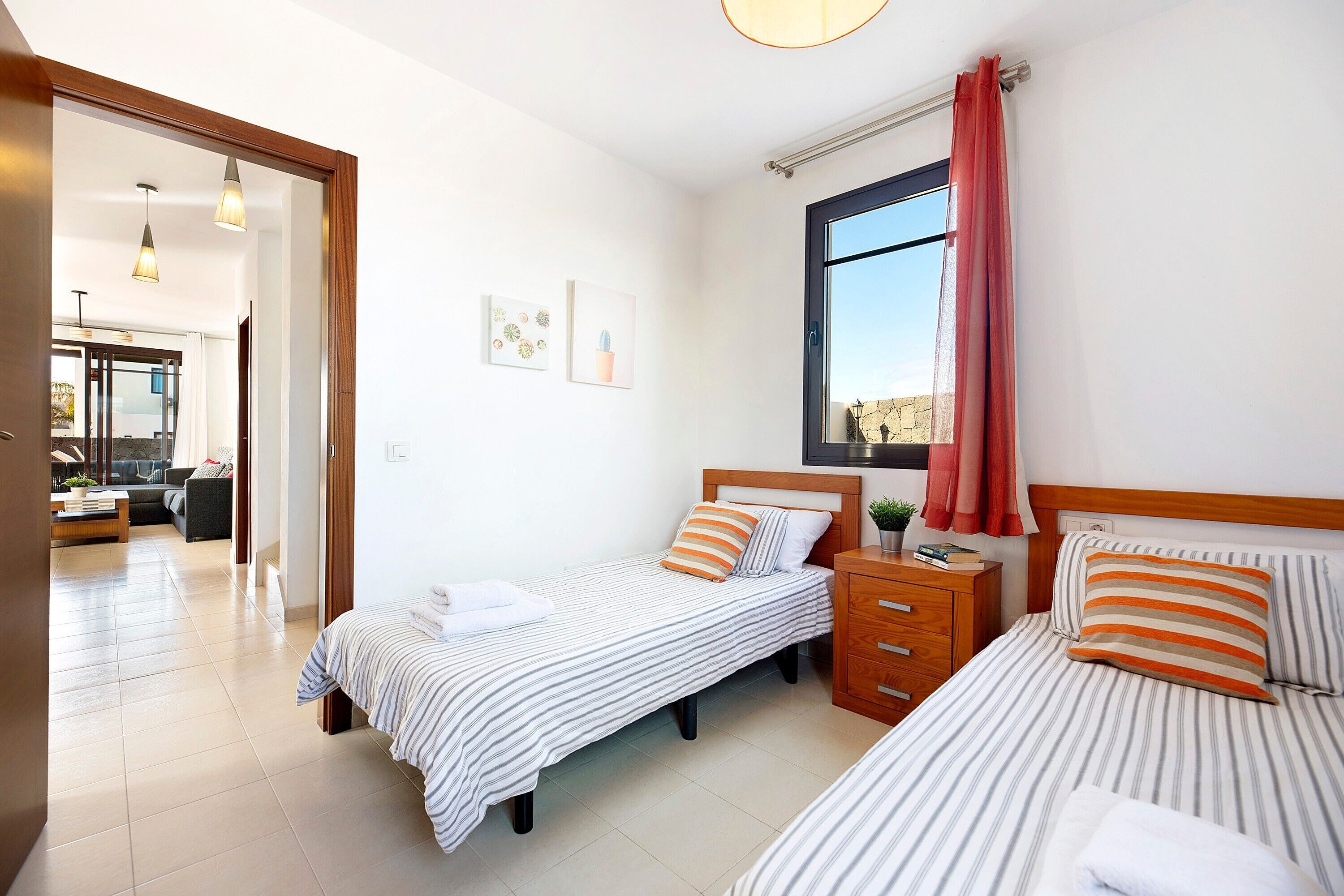 A hotel room with two beds, a wooden nightstand, a window with curtains, and a view of the outside.
