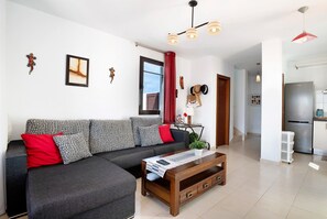 Una sala de estar moderna con un sofá modular, una mesa de centro y una cocina visible al fondo.