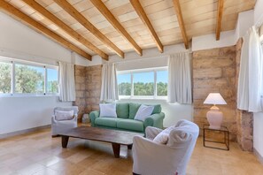 Amplia sala de estar con techo de madera, ventanas grandes, un sofá verde, dos sillones, una mesa de centro y una lámpara.