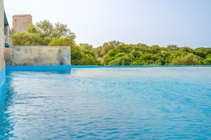 A swimming pool with a stone wall and greenery in the background.