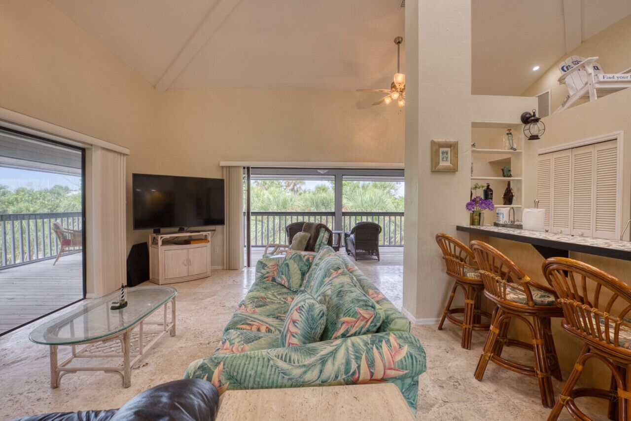 A spacious living area with a large sofa, a glass coffee table, and a TV. There are wicker chairs and a dining area with a bar.