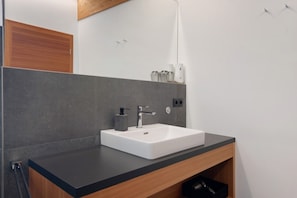 Une salle de bain moderne avec un lavabo blanc, un plan de travail foncé et des meubles en bois.
