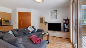 Una sala moderna con un sofá gris, un televisor de pantalla plana, una estantería y una puerta de madera.