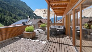 Terraza de madera con mobiliario exterior, un pérgola y vistas a una montaña boscosa.