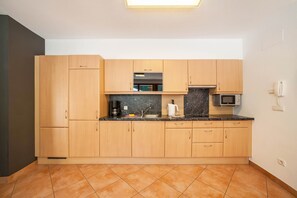 A modern kitchen with wooden cabinets, a marble countertop, a built-in oven, and a microwave.