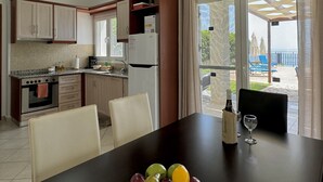 A kitchen with a dining area, a refrigerator, and a view of a pool and beach. - Villa Sakos (Skala)