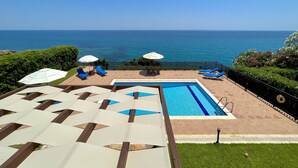 A pool area with a view of the ocean, lounge chairs, and umbrellas. - Villa Sakos (Skala)