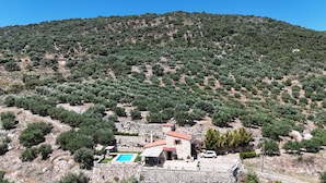 Villa de piedra con piscina, rodeada de olivares y con montañas al fondo.