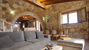 Una sala de estar con paredes de piedra, un sofá gris, una mesa de centro de madera, y un comedor con sillas y una mesa.