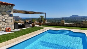 Una piscina con un muro de piedra y una zona de estar techada.