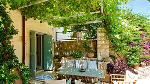 Un espace extérieur aménagé dans un style rustique, avec un mur en pierre, une table, des chaises et des plantes en pot.