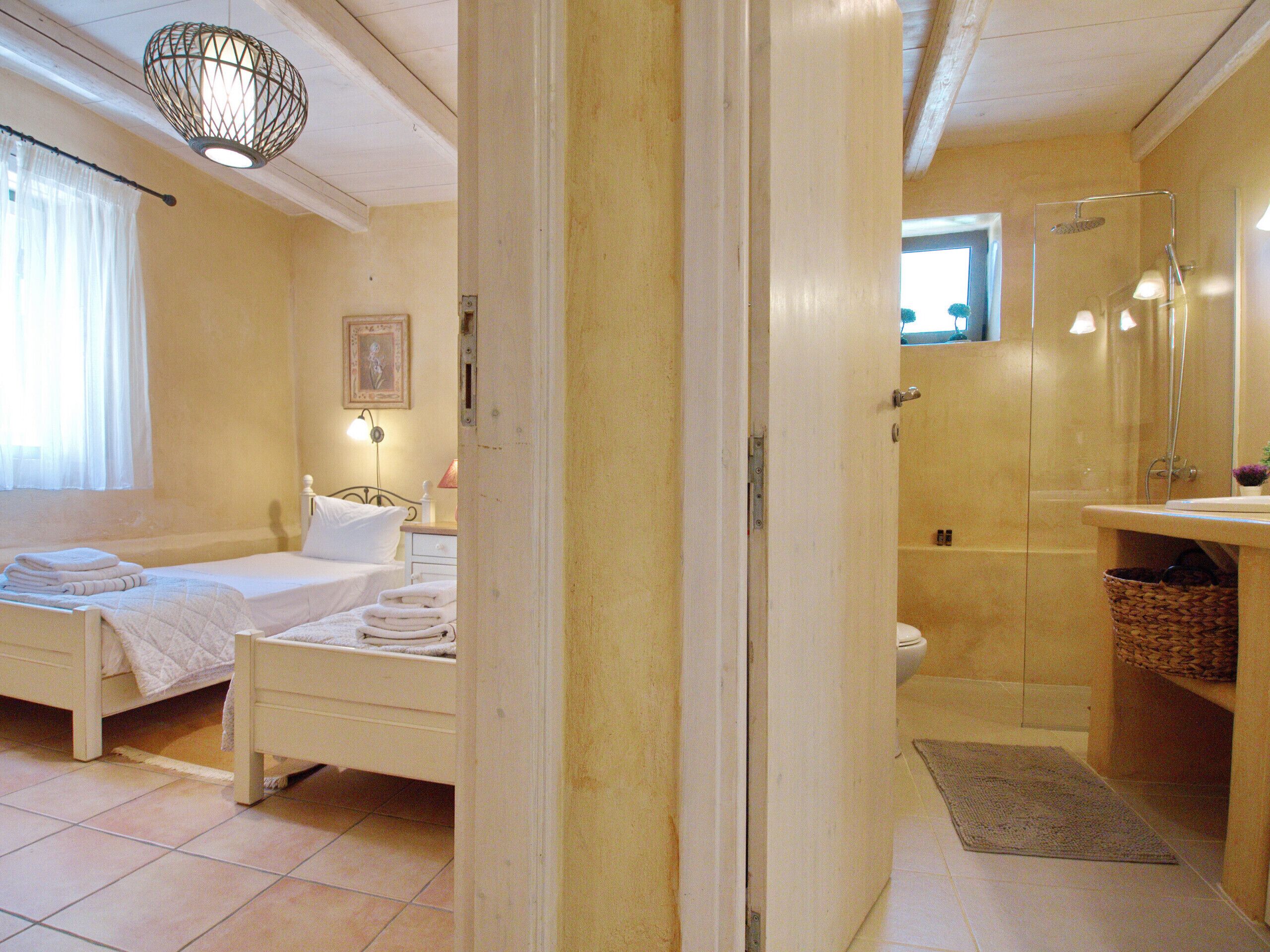 A bedroom with a bed, bedside table, and a nightstand. There is a bathroom with a shower, sink, and toilet.
