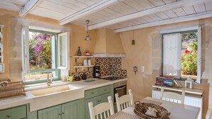 Une cuisine avec un plafond en bois, des armoires vertes, un plan de travail blanc et une fenêtre donnant sur un jardin fleuri.