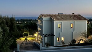 Una casa moderna con tetto in tegole, un piccolo giardino con una palma e vista sul mare al crepuscolo.