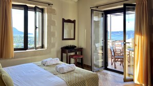 Ein Hotelzimmer mit Bett, Schreibtisch und Meerblick durch eine Glastür.