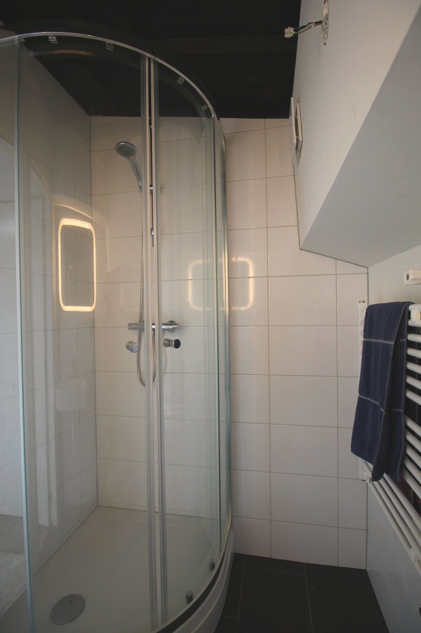 Eine gläserne Dusche mit weiß gefliesten Wänden und einem Handtuchhalter mit Handtuch.