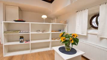 Una habitación con una estantería blanca, una mesita con un jarrón de girasoles y una ventana con cortina.