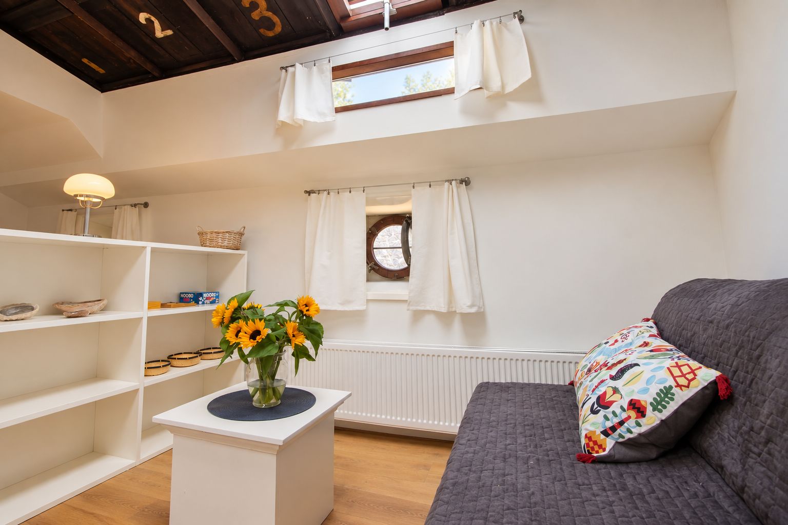 Een gezellige woonkamer met een bank, een klein bijzettafeltje met een vaas zonnebloemen, en een raam met gordijnen.