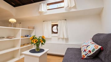 Een gezellige woonkamer met een bank, een klein bijzettafeltje met een vaas zonnebloemen, en een raam met gordijnen.