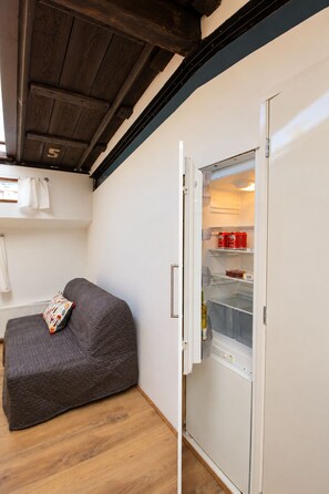 A compact living space with a kitchenette area, including a refrigerator and a small sofa. - Cosy houseboat studio in the old city center (Amsterdam)