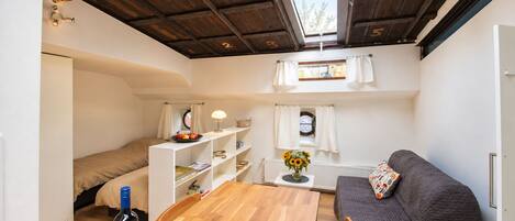 A compact room with a bed, a sofa, a table, and a window.