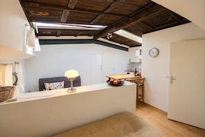 A compact kitchen with a dining table, a clock on the wall, and a ceiling with exposed beams.