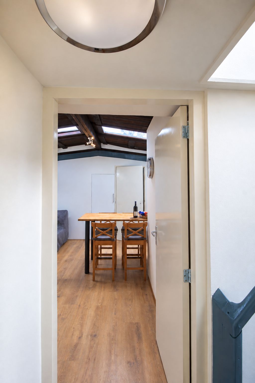 A room with a wooden dining table and chairs, a white door, and a view of a ceiling with exposed beams.