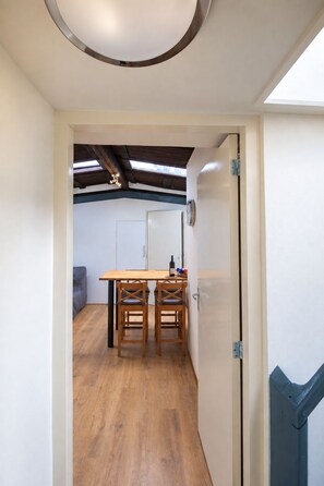Une pièce avec une table et des chaises de salle à manger en bois, une porte blanche et une vue sur un plafond avec des poutres apparentes.